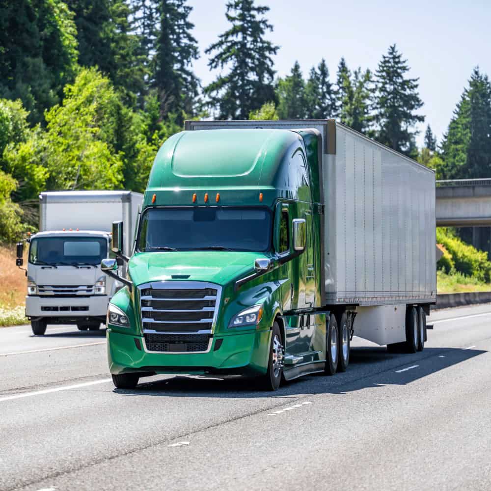 Green semi truck driving on highway with trees in background.