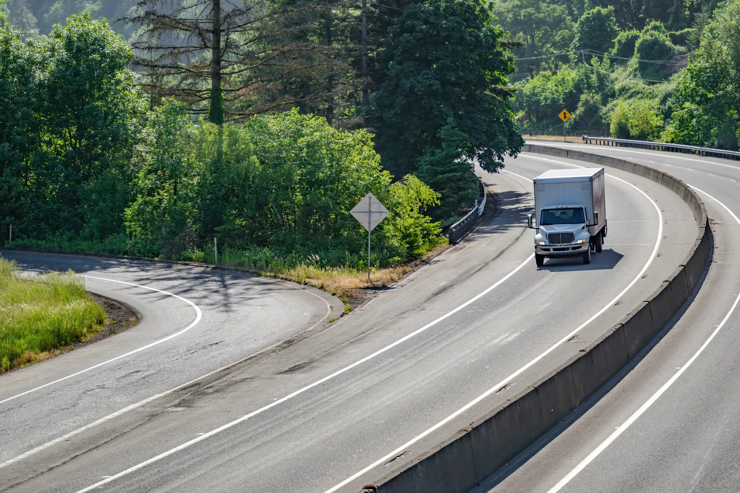 Box truck driving on winding highway surrounded by greenery in Texas.